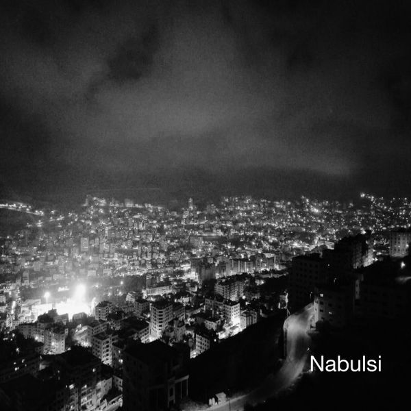 Nablus at night. Photographed from a vantage point on the hills of Jabal Jirzim a sprawl of illuminated appartment blocks and other buildings fill the lower half of the scene. Above, smokey clouds. The combination of black and white and cloud gives much of the image a slight haze. The word Nabulsi is rendered in the bottom right corner.